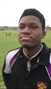 young player in his blac, white and purple school football kit stands proudly looking off camera